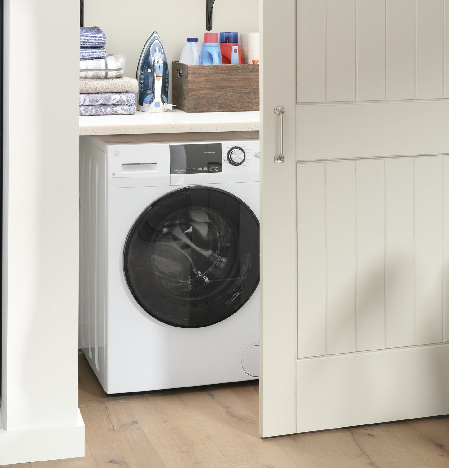 White front load washer dryer combo in nook with countertop, iron, folded towels, and laundry supplies nearby