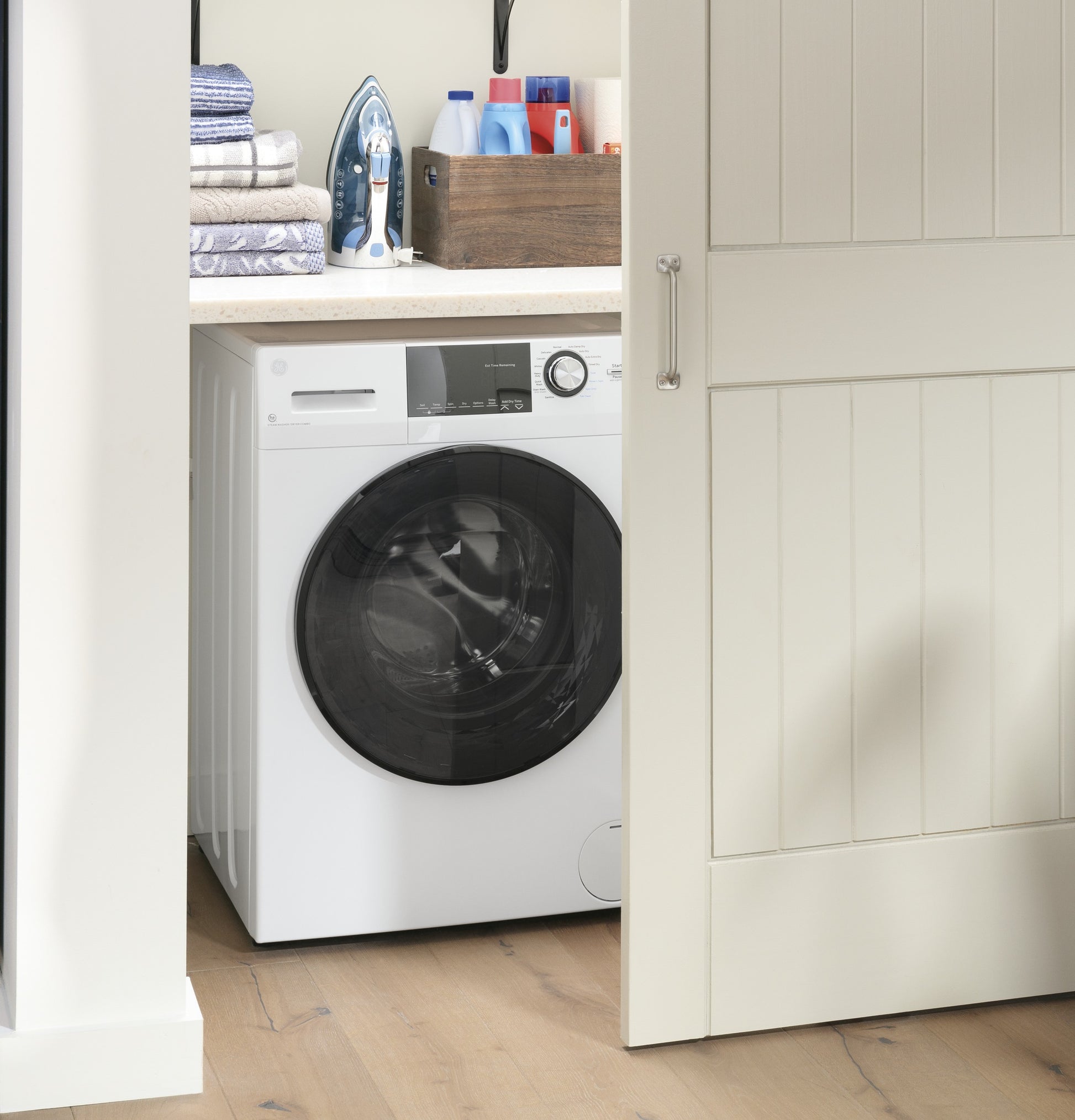 White front load washer dryer combo in nook with countertop, iron, folded towels, and laundry supplies nearby