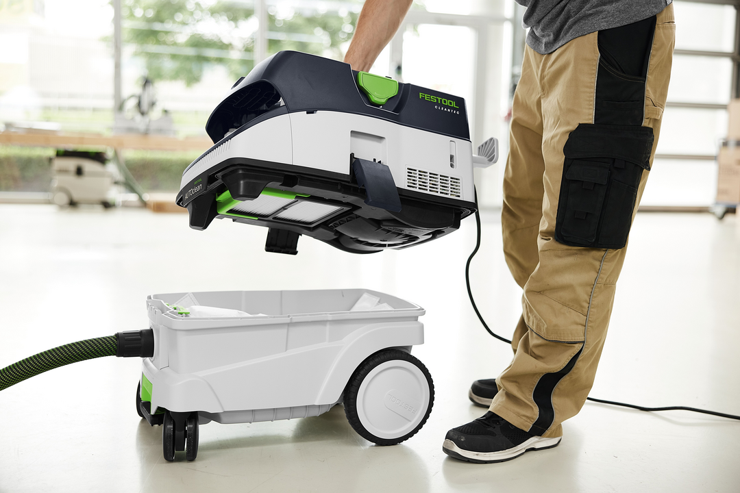 Person lifting top unit of Festool dust extractor from wheeled base for portable dust collection in workshop