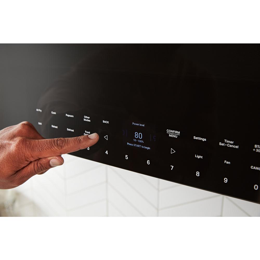 Close-up of finger pressing digital control panel on black built-in over-the-range air fry microwave from kitchen appliances