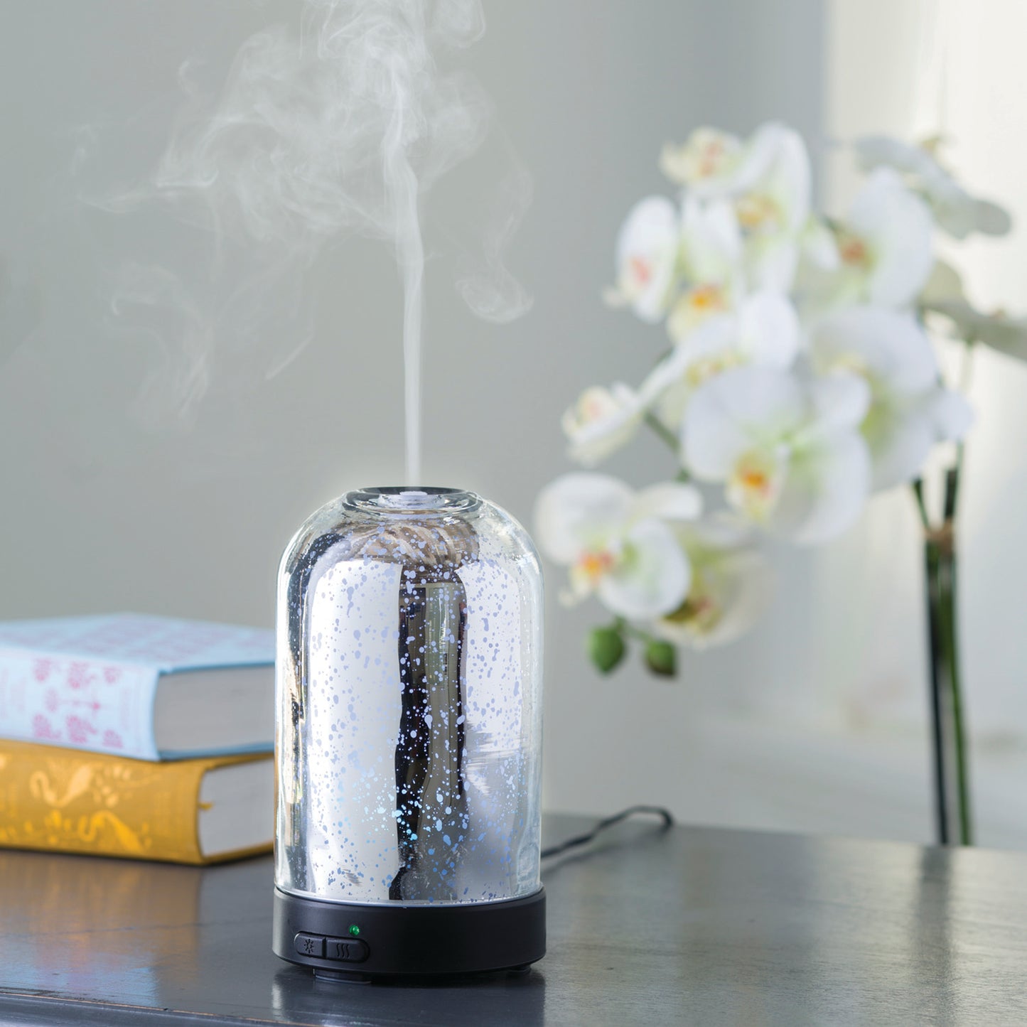 Medium mercury glass diffuser with silver dome and mist, set on table with books and floral decor in home setting