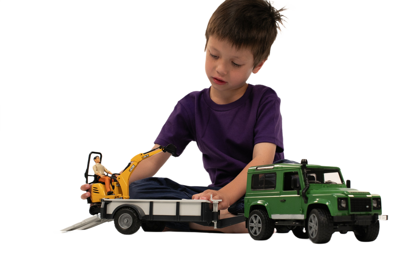 Child playing with green Bruder Toys Land Rover Defender hauling a trailer carrying yellow JCB micro excavator toy