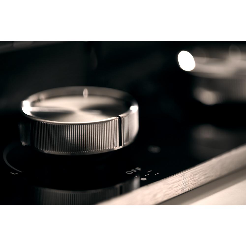 Close-up of a metallic control knob on a black gas-on-glass cooktop for kitchenware and home improvement tools.