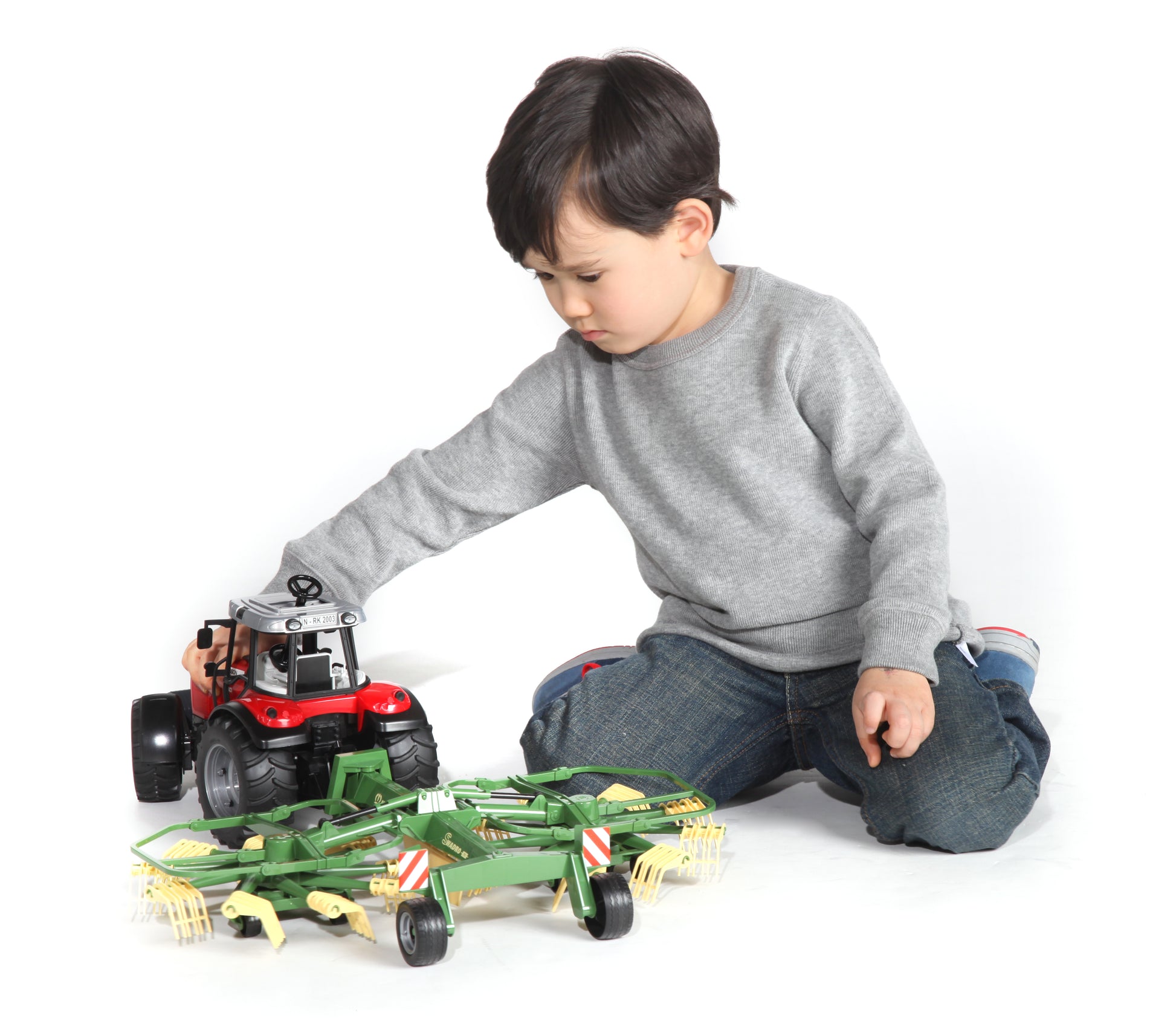 Child playing with red tractor and green dual rotary swath windrower toy from Bruder Toys and Vehicles collections