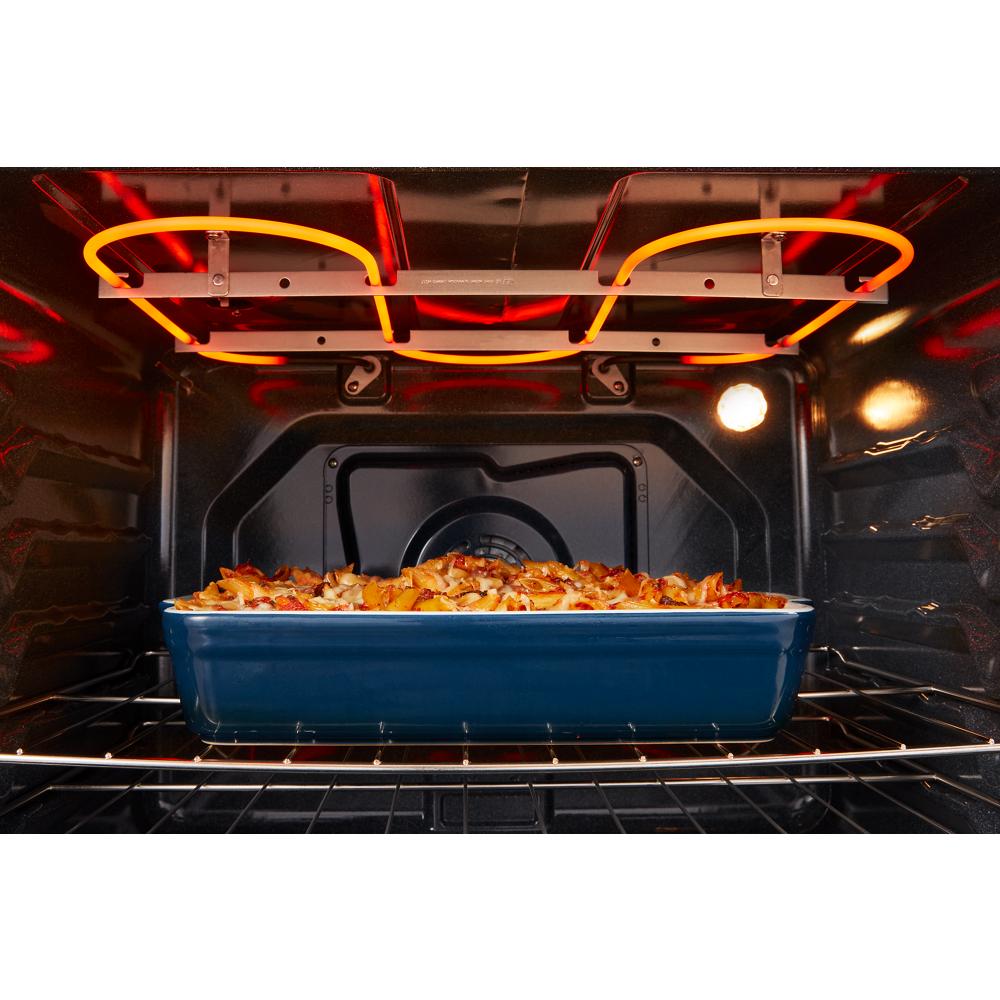 Blue ceramic baking dish with casserole cooking on the wire rack inside an electric oven cavity with glowing heating elements