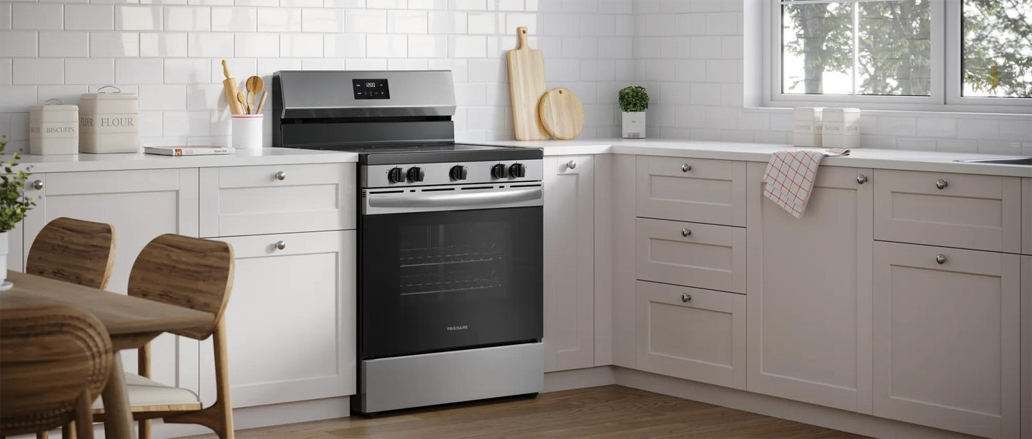 Freestanding electric range with five burners and digital display in a bright kitchen with white cabinetry and wood flooring