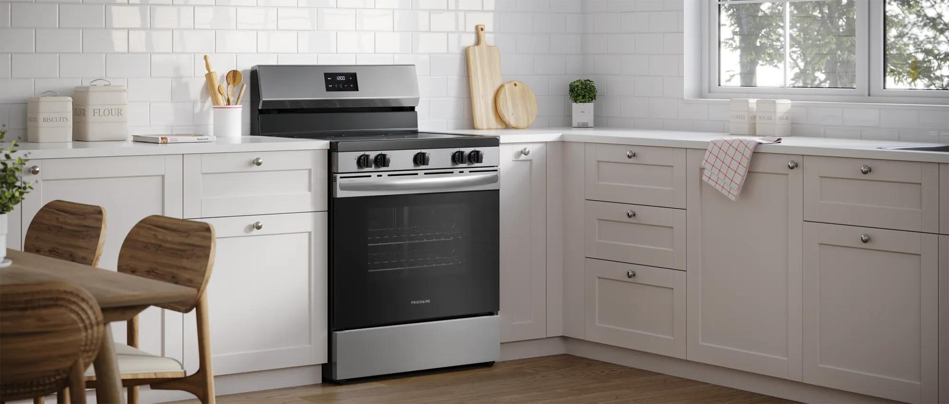 Freestanding electric range with five burners and digital display in a bright kitchen with white cabinetry and wood flooring
