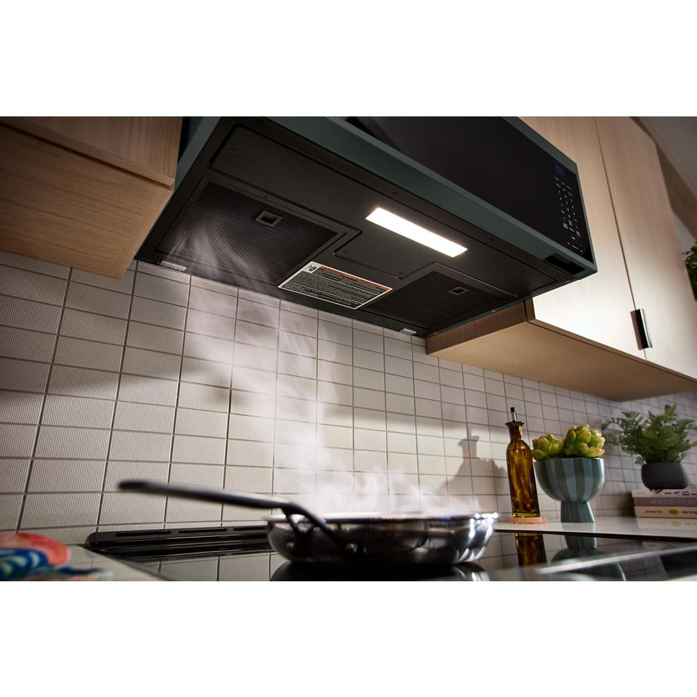 Black low profile microwave hood with dual fan ventilation clearing steam above stovetop in modern kitchen setting