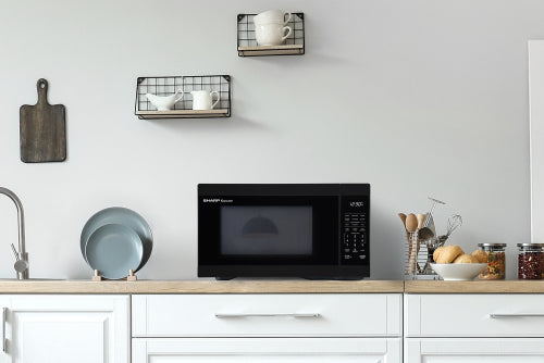 Black countertop microwave oven on wooden kitchen counter with white cabinets and minimalist decor