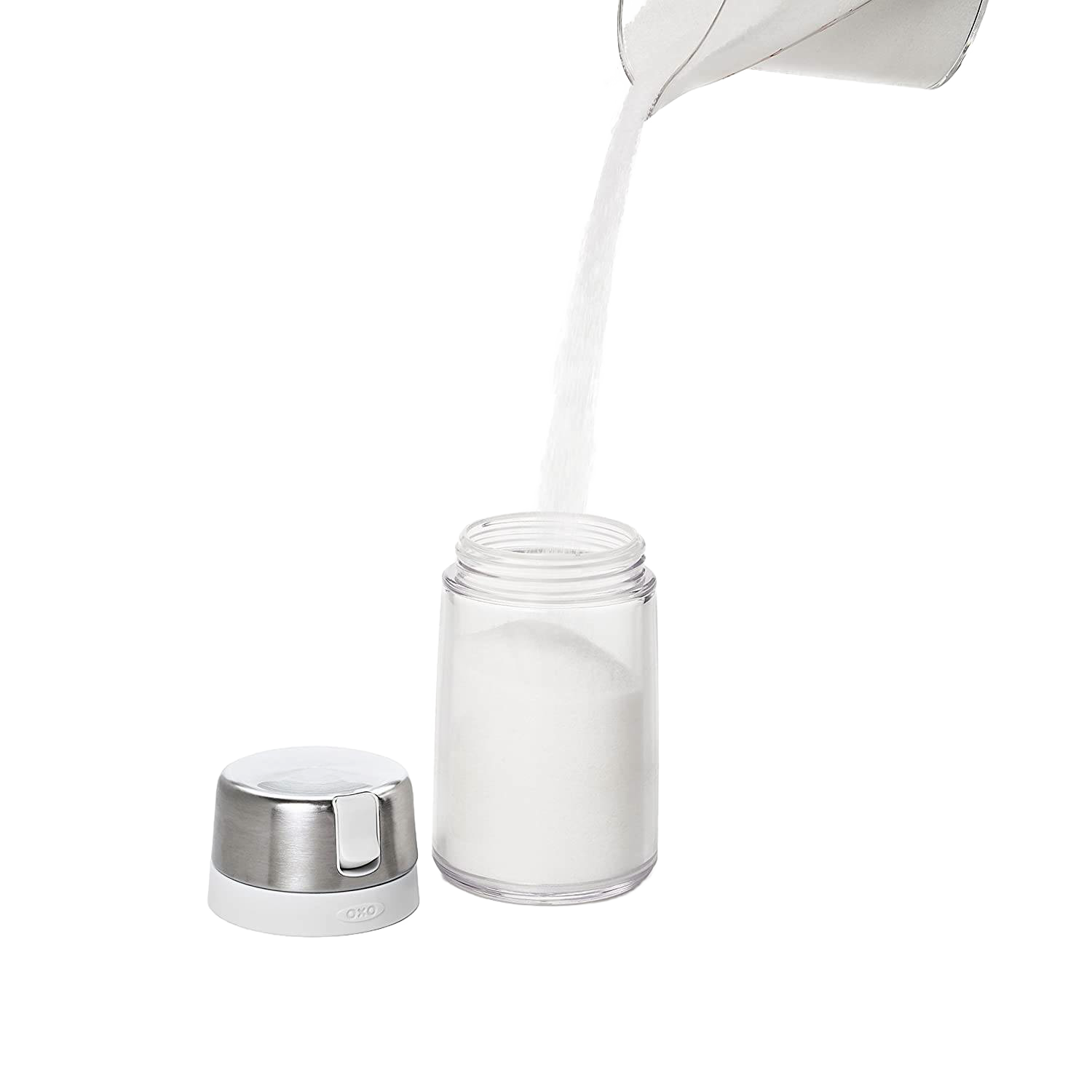 Clear OXO sugar dispenser with stainless steel lid and white spout with sugar pouring into container for kitchen storage