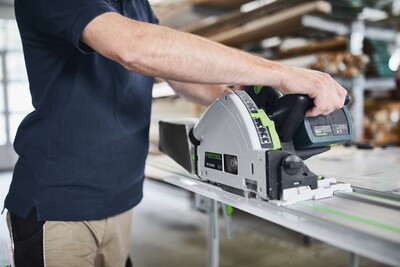 Person using Festool cordless track saw with guide rail cutting wood on workbench in electric power tools workshop