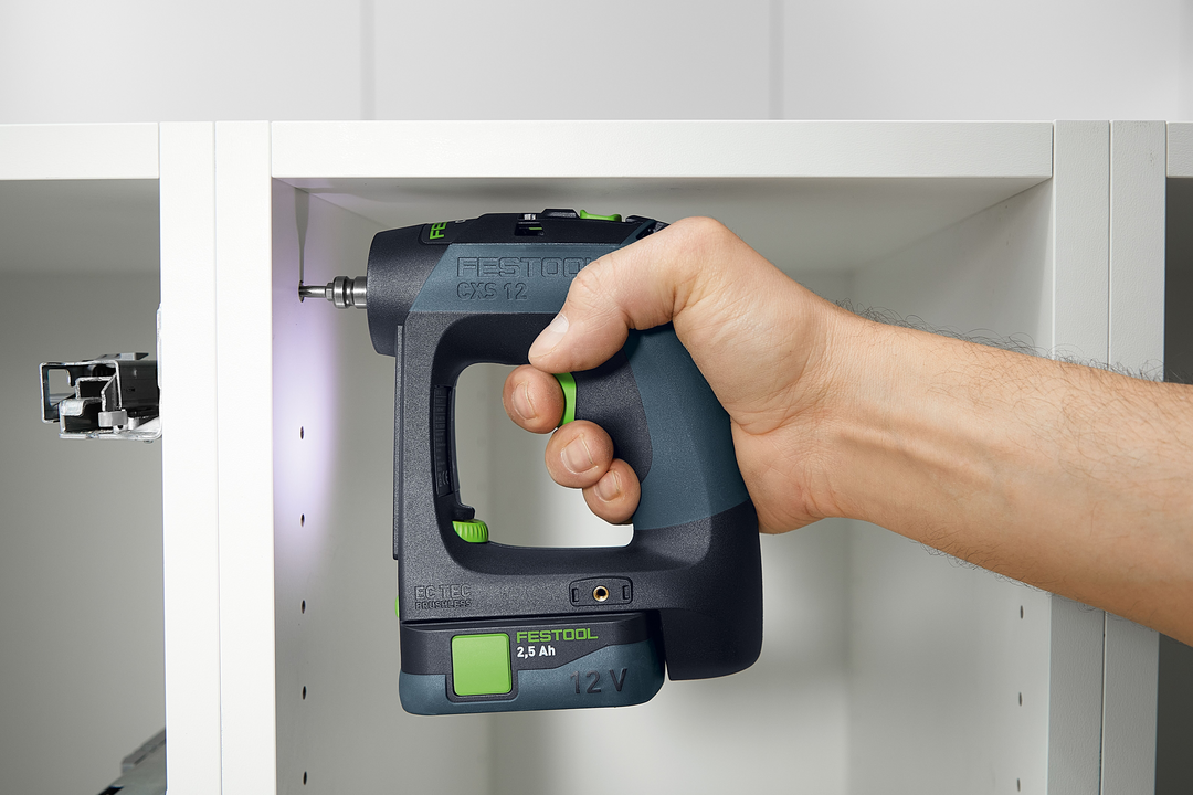 Hand using compact Festool cordless drill with ergonomic grip to assemble white shelving unit in woodworking setting