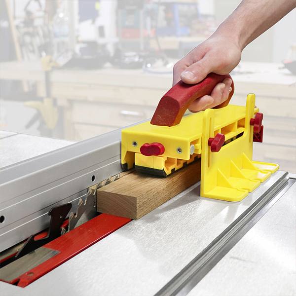 Hand using yellow and red push block to guide wood through table saw for safe woodworking projects