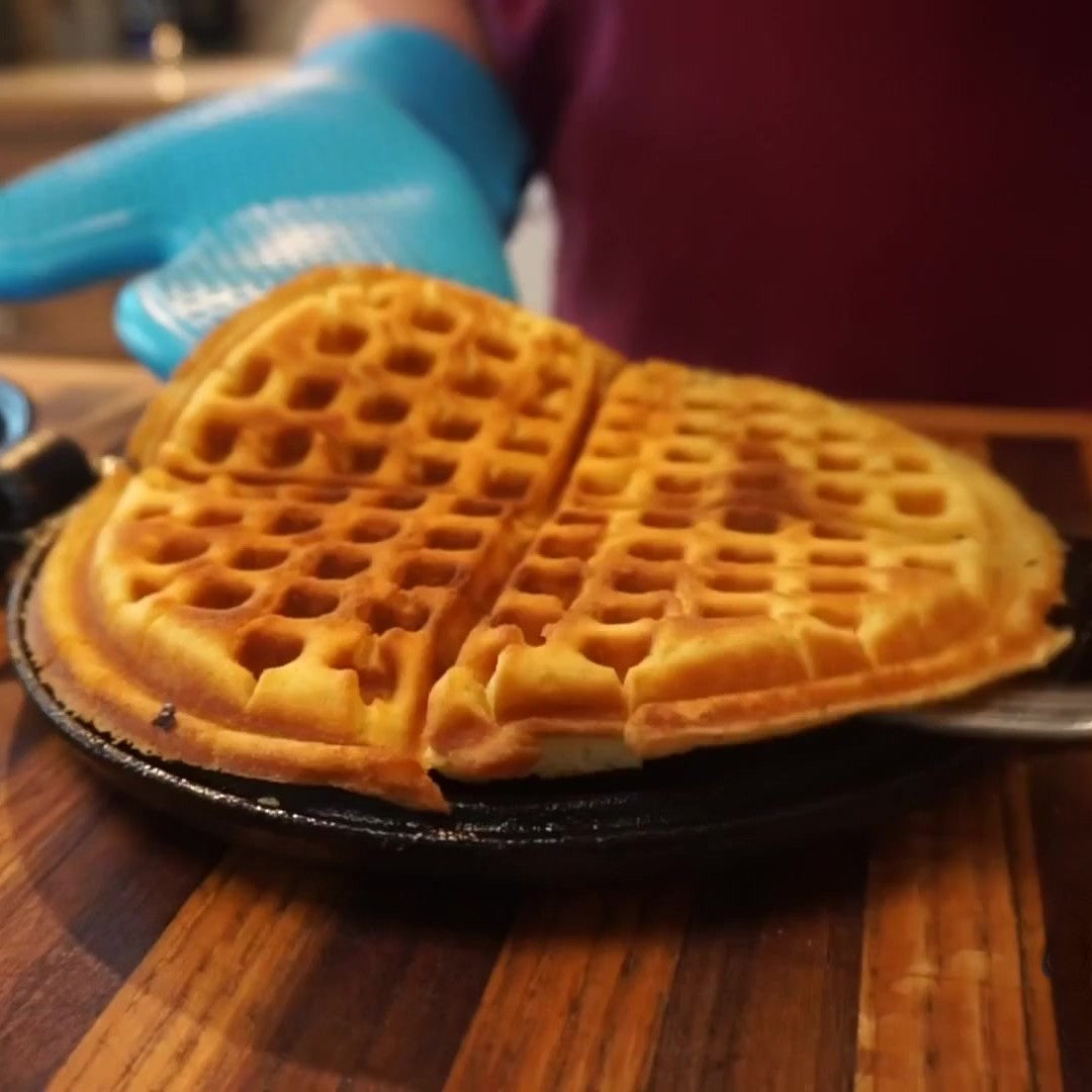 Golden heart-shaped waffle freshly cooked in cast iron stovetop waffle maker on wooden kitchen surface