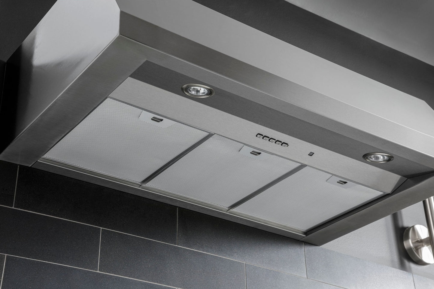 Stainless steel commercial style kitchen hood with built-in lights and mesh filters for ventilation and appliances.