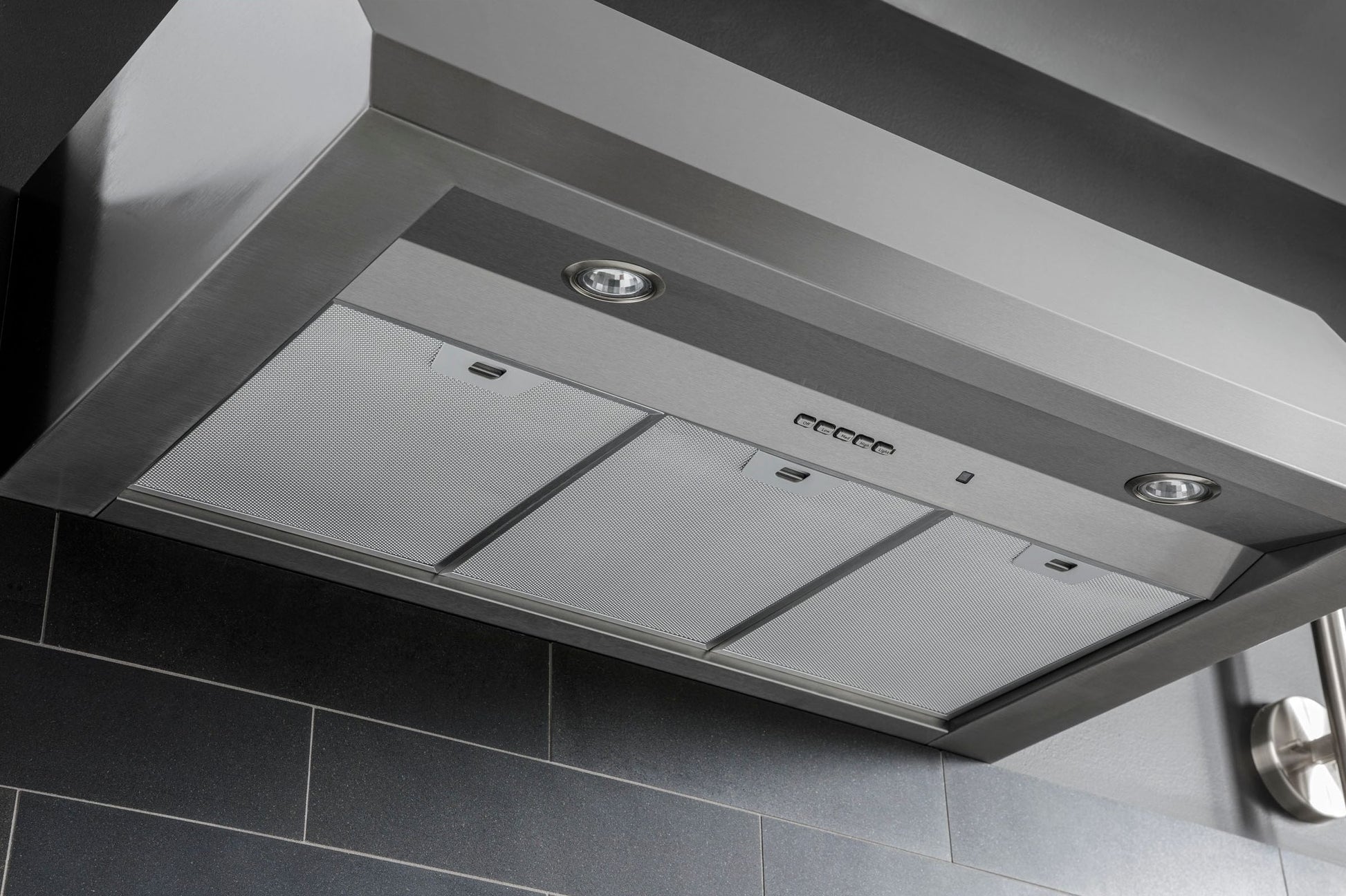 Stainless steel commercial style kitchen hood with built-in lights and mesh filters for ventilation and appliances.