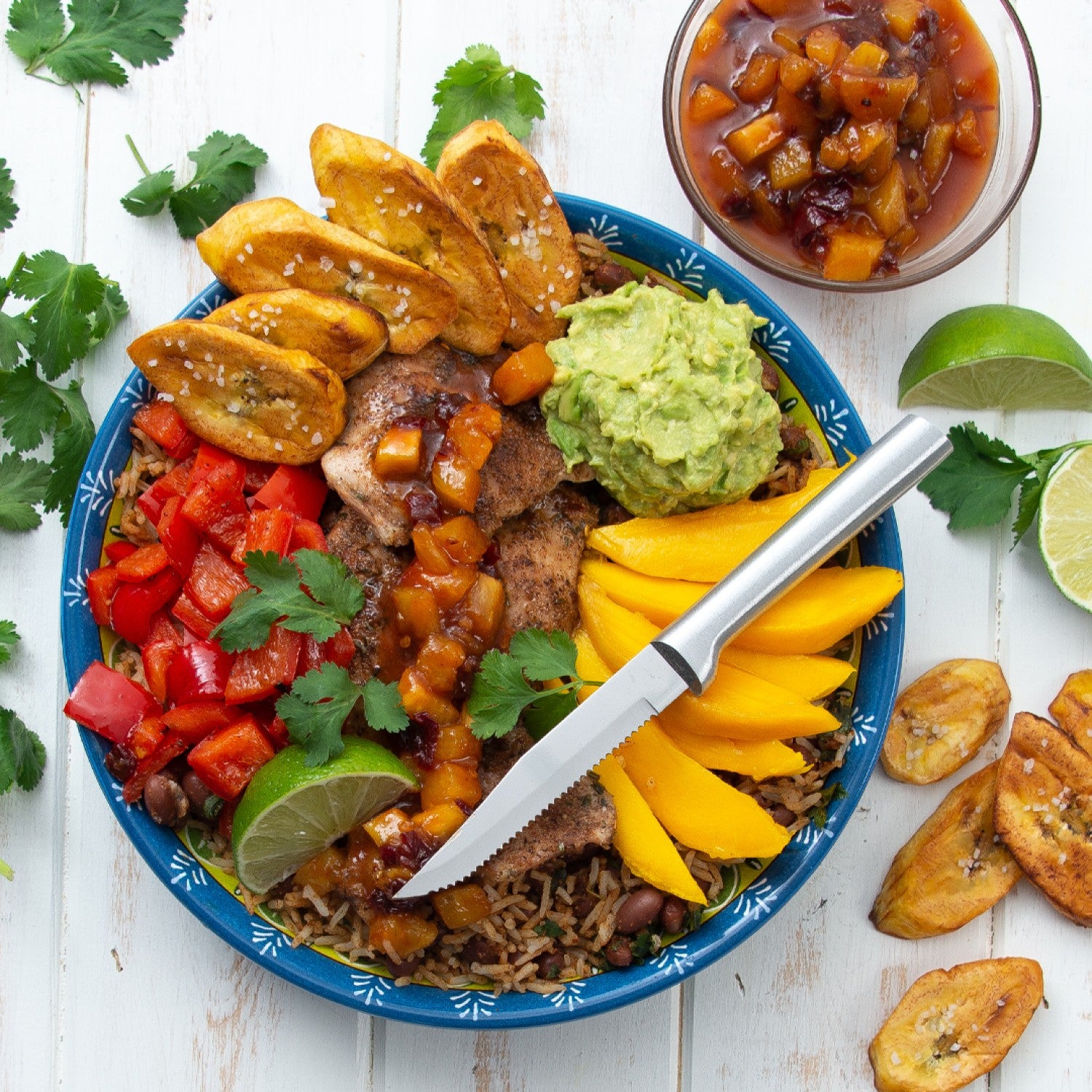Serrated steak knife with a solid aluminum handle resting on a vibrant plate with seasoned meat, mango slices, guacamole, red peppers, plantains, and cilantro, ideal for Kitchenware and Cooking Utensils collections under $50.