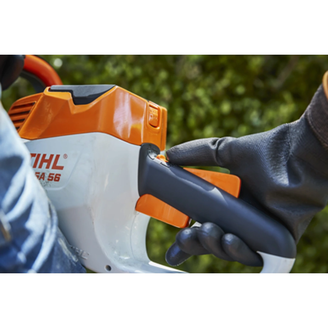 Close-up of gloved hand pressing trigger on orange and white STIHL HSA 56 cordless hedge trimmer handle for home improvement tasks