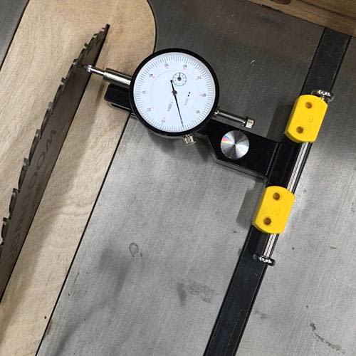 Dial indicator with yellow mounts measuring alignment on a saw blade for precision in tool and saw accessories collections
