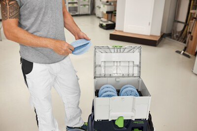 Person organizing blue abrasive discs inside an open Festool tool storage box for workshop organization and home improvement tools