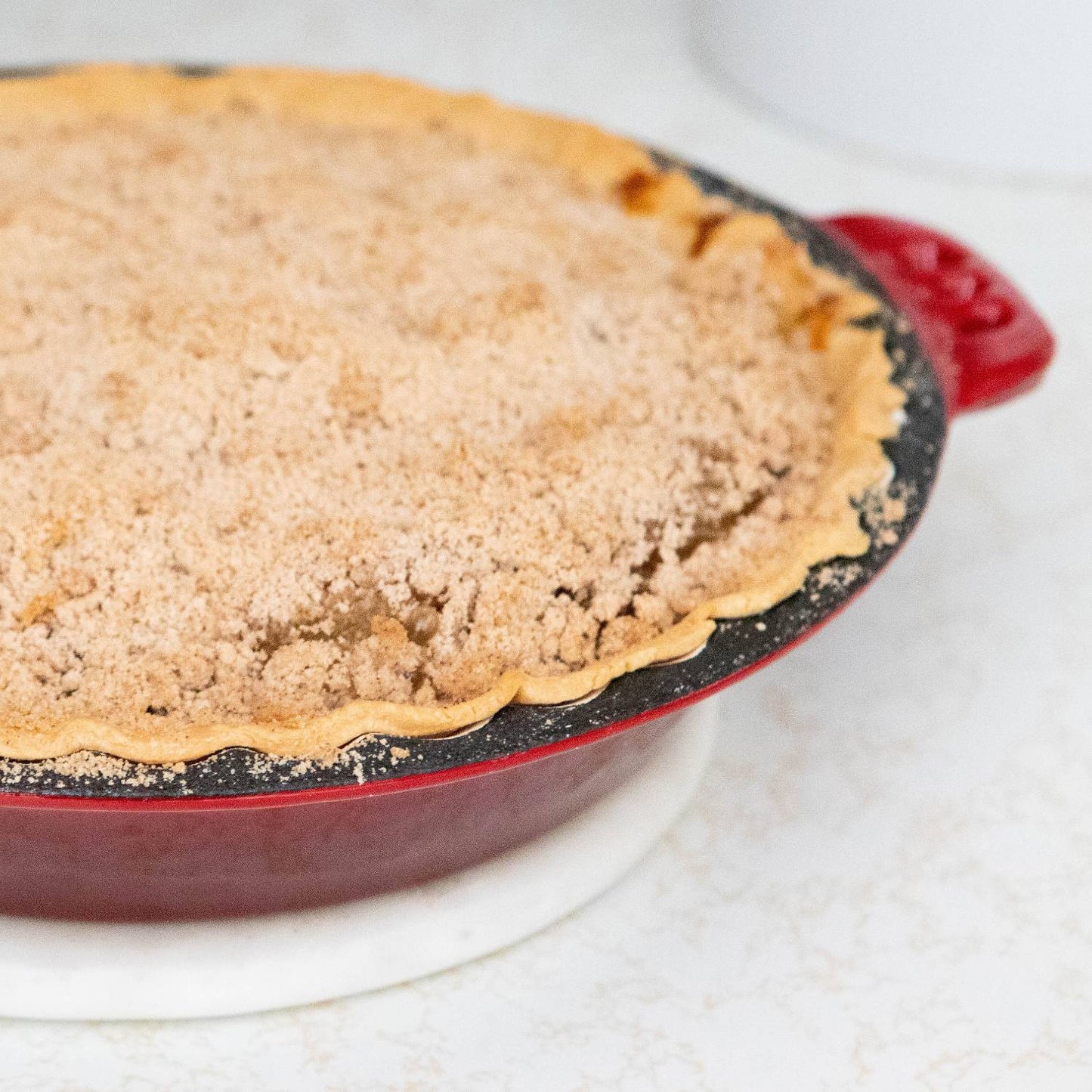 Freshly baked crumb-topped pie in red cast iron pan with crimped edges on white kitchen countertop under $50 collection