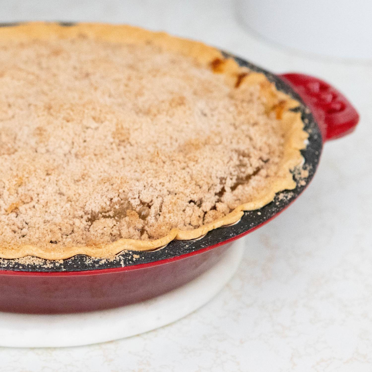 Freshly baked crumb-topped pie in red cast iron pan with crimped edges on white kitchen countertop under $50 collection