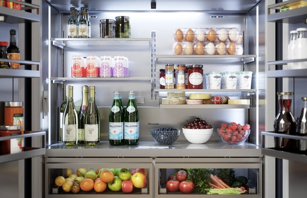 Open French door bottom freezer refrigerator showing organized shelves with beverages, eggs, fruit, and vegetables