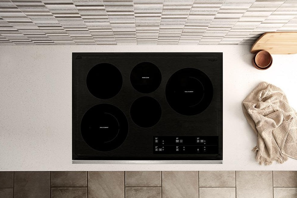 Black electric ceramic glass cooktop with five radiant elements and digital touch controls on kitchen countertop
