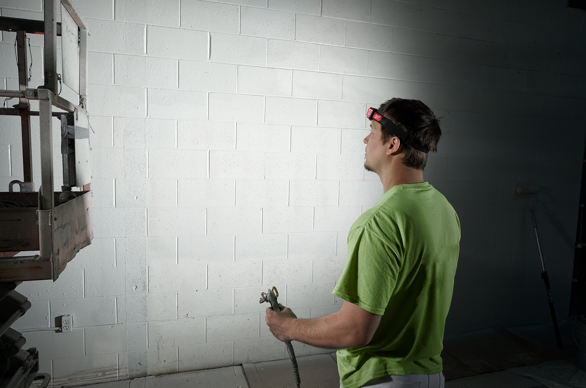 Man wearing a Milwaukee red and black adjustable headlamp illuminating a brick wall during home improvement work