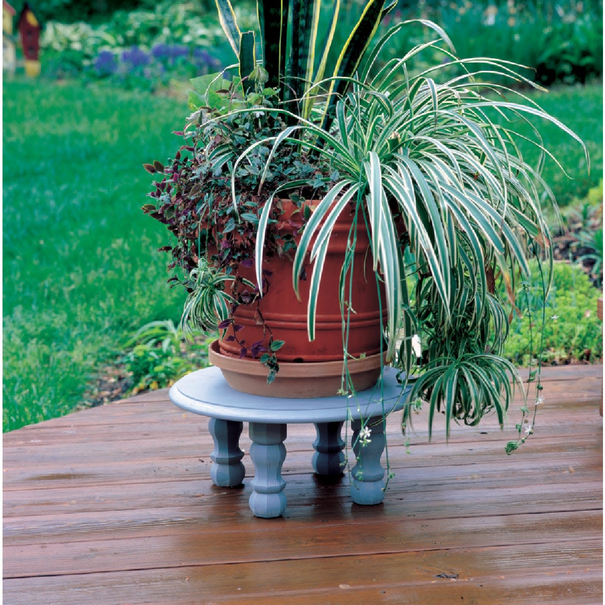 Round wooden stand painted soft gray holding large vibrant green potted plants on outdoor wood deck surface