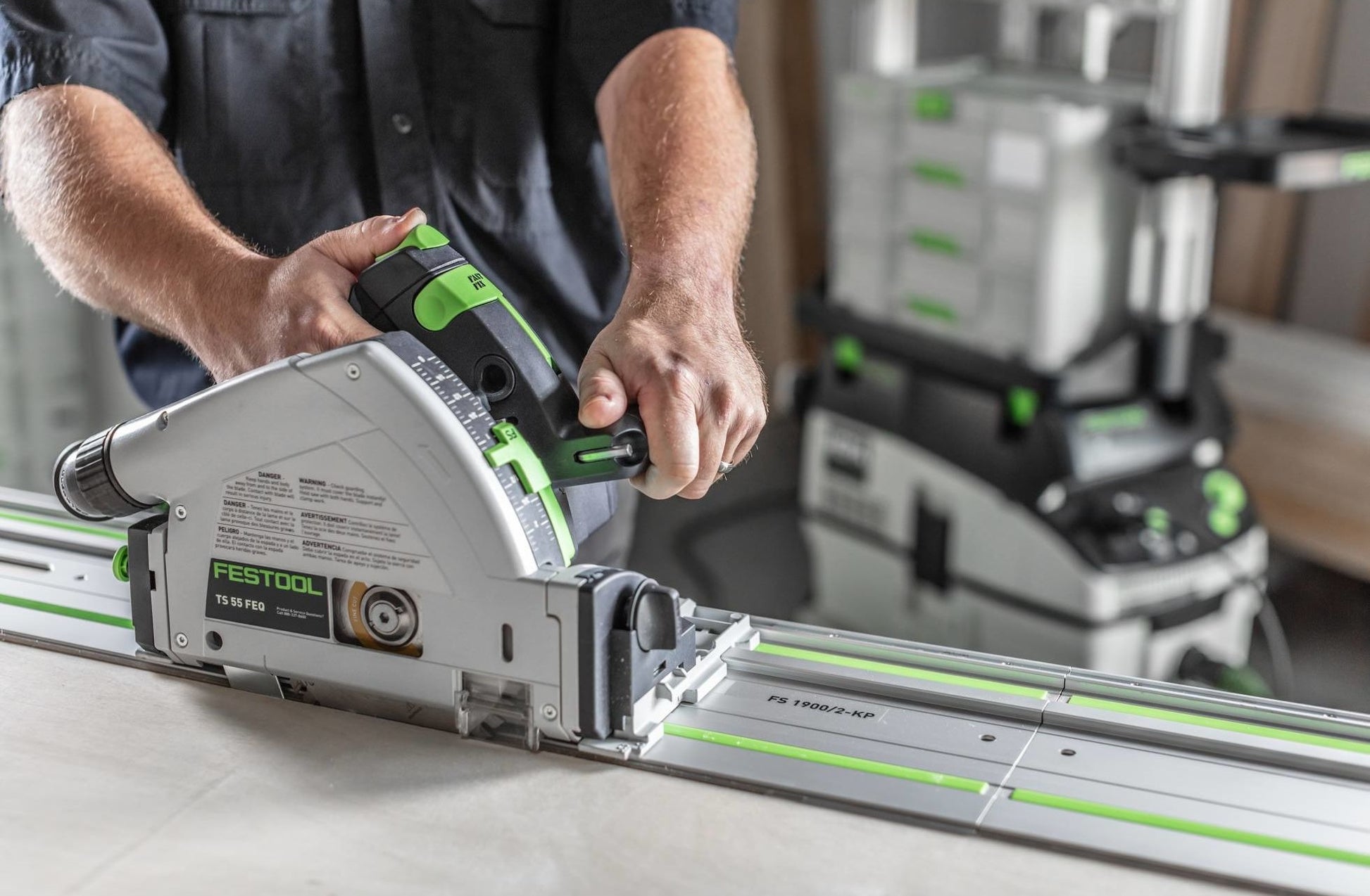 Person operating Festool plunge-cut track saw on guide rail on workbench in workshop with tools nearby