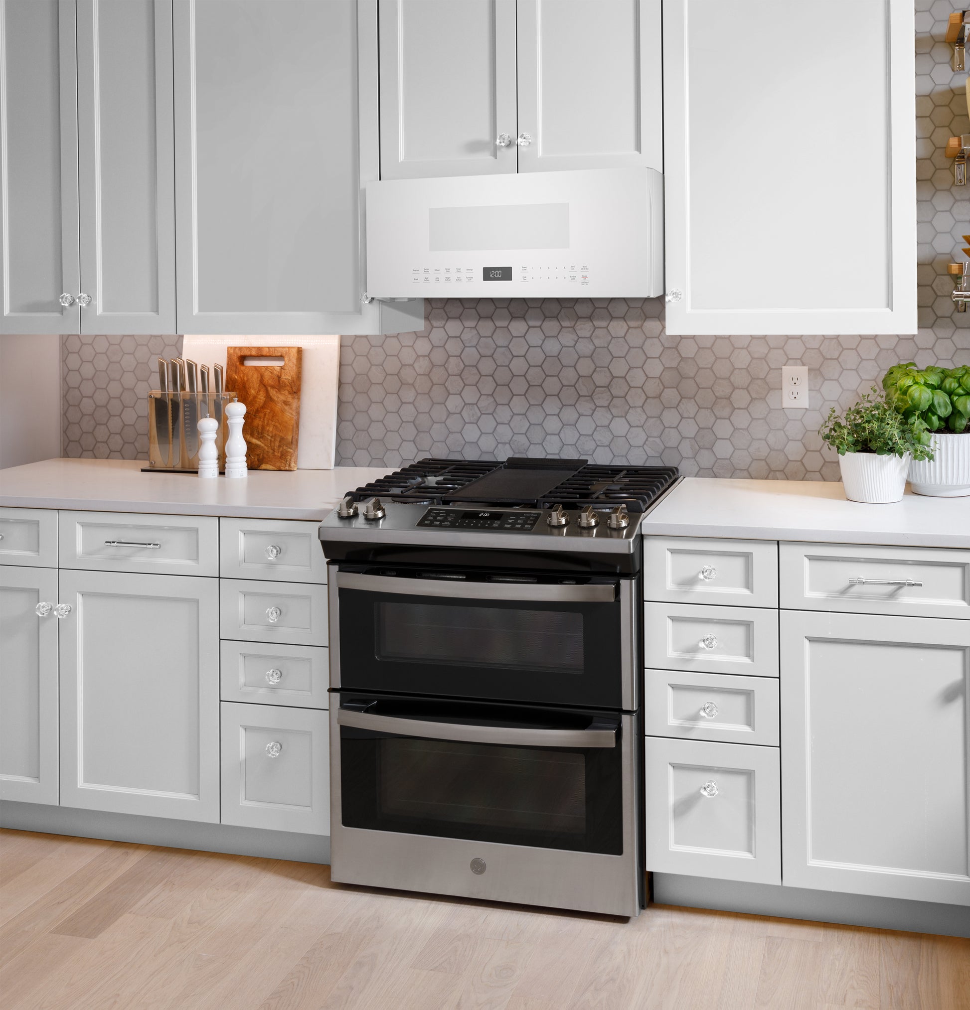 Modern kitchen with white cabinetry, hexagonal tile backsplash, stainless steel double oven, and low profile sensor microwave above
