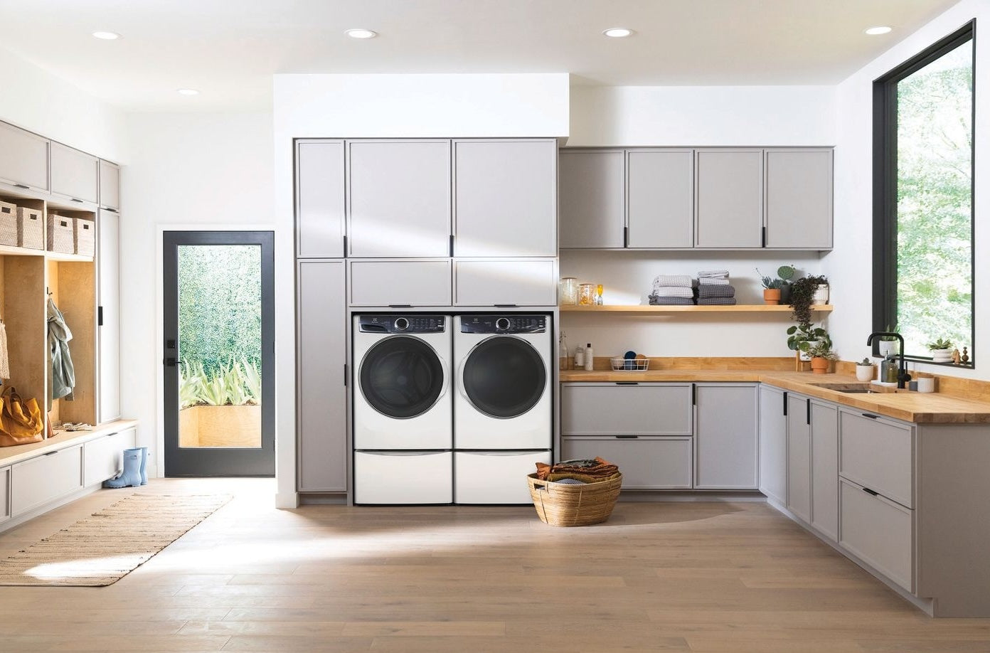 Modern laundry room with front load electric dryer, gray cabinetry, wood countertops, and natural light from large window