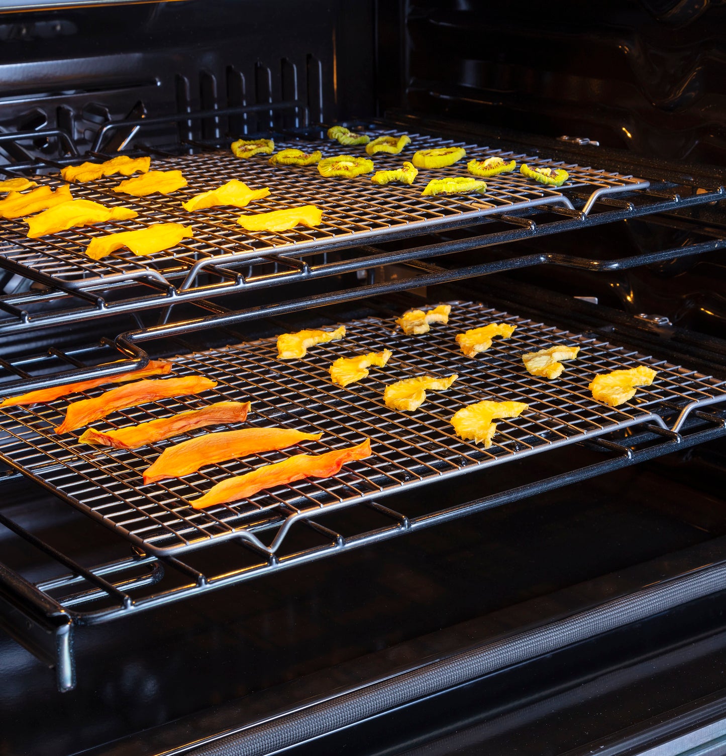 Open convection double wall oven with wire racks drying slices of bell pepper and other vegetables inside appliance