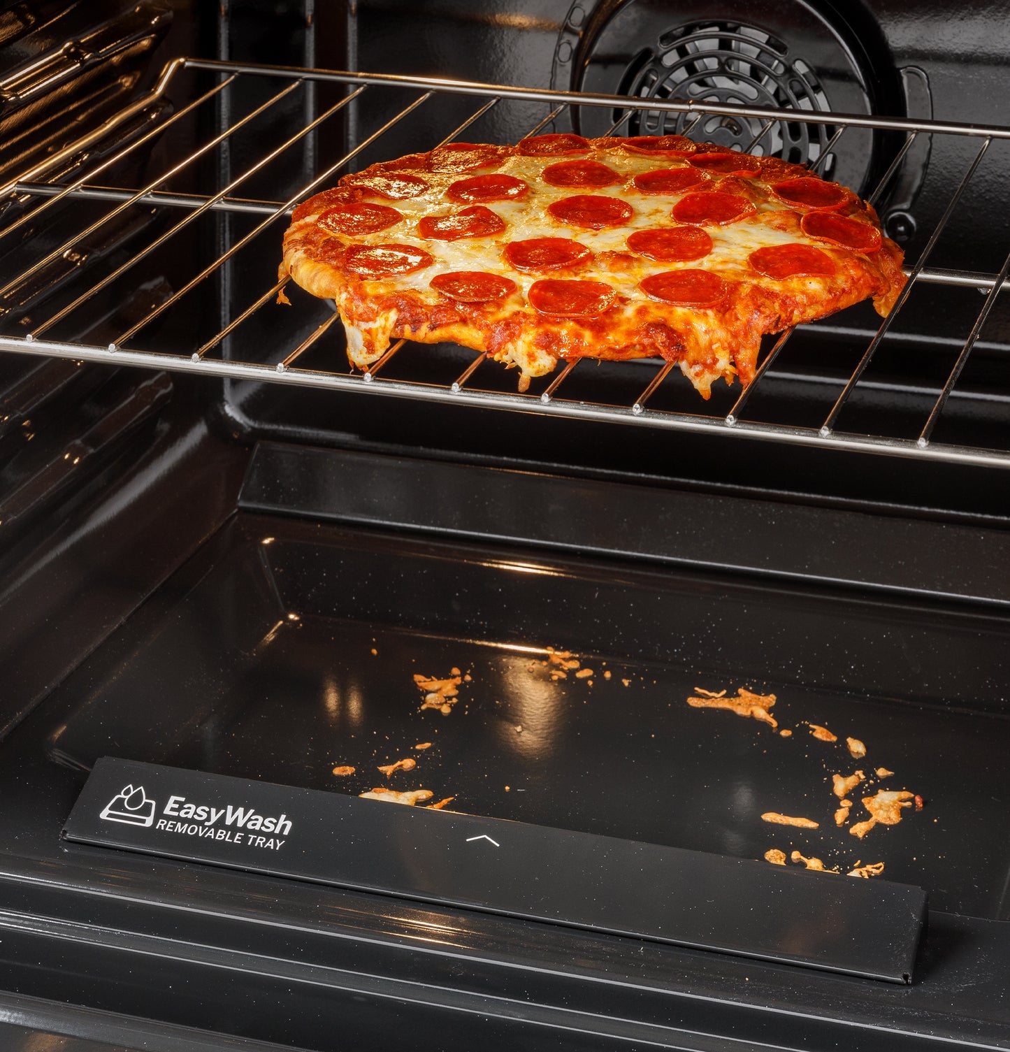 Pepperoni pizza baking on rack above EasyWash removable tray inside electric convection range oven cavity