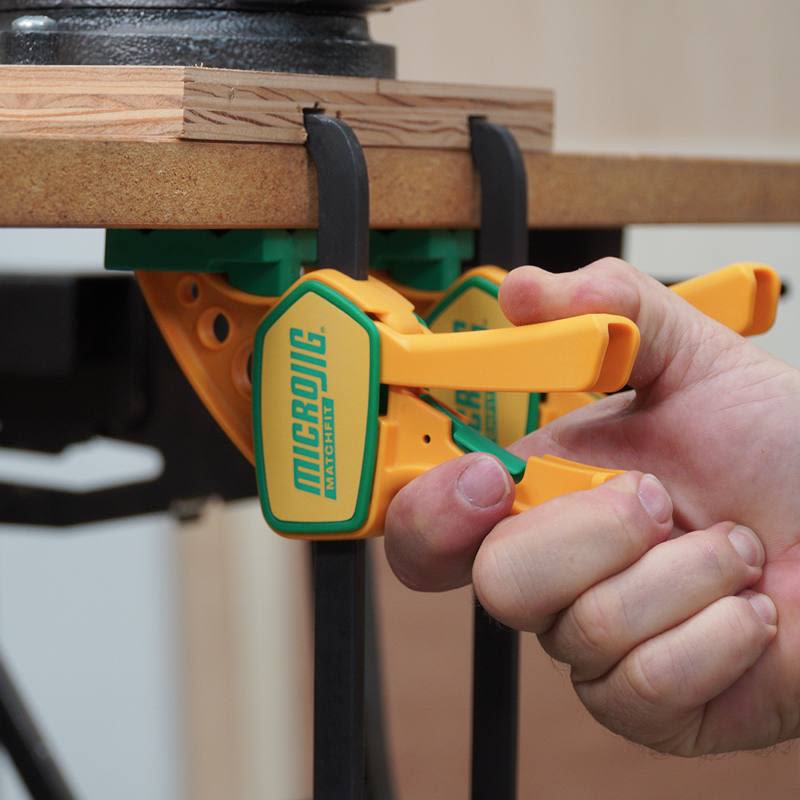 Hand tightening yellow and green Microjig clamps securing wood on a workbench in tool and saw accessories collections