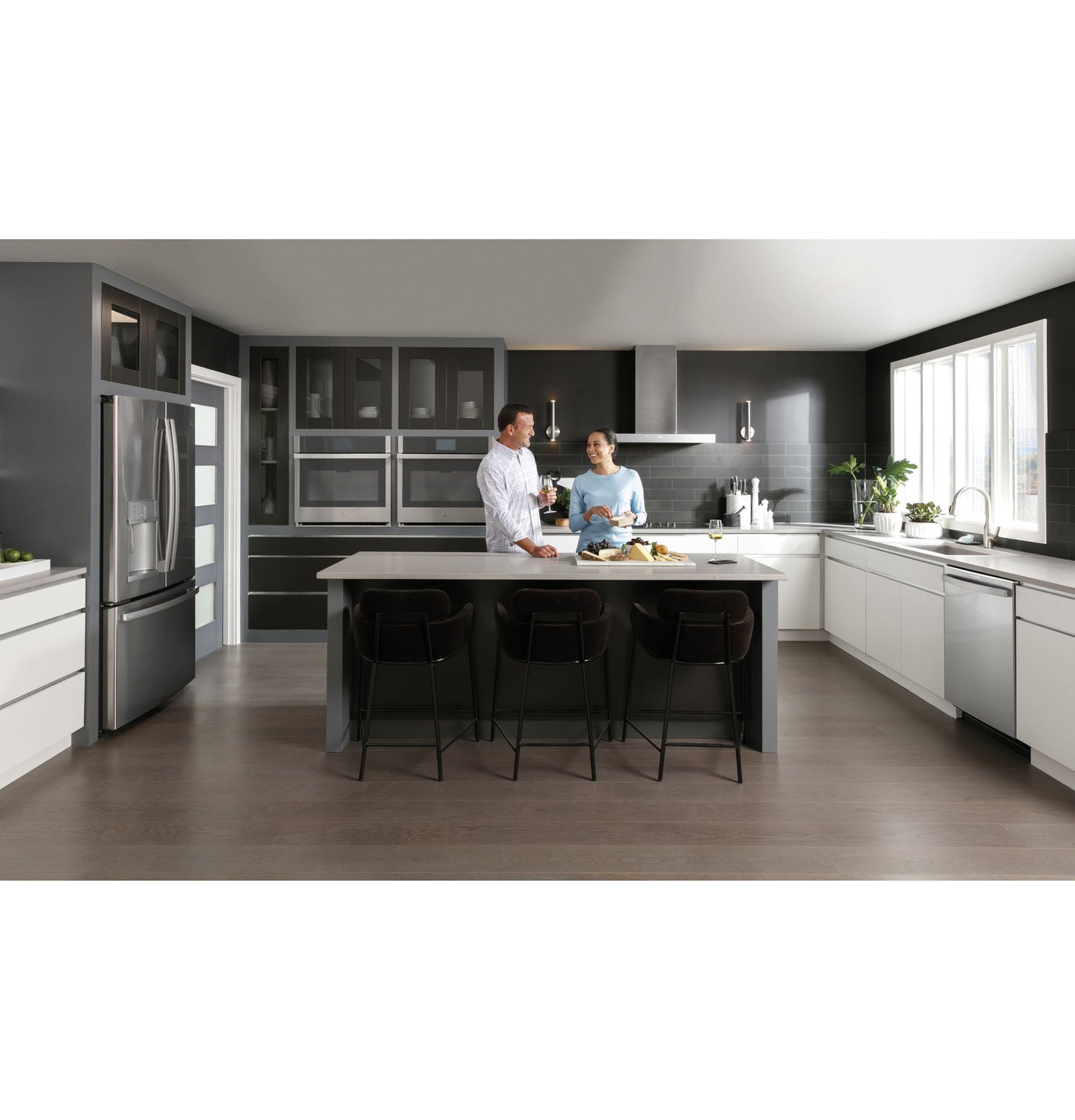Modern kitchen with dark cabinetry and white countertops featuring a smart 36-inch wall mount hood and stainless appliances