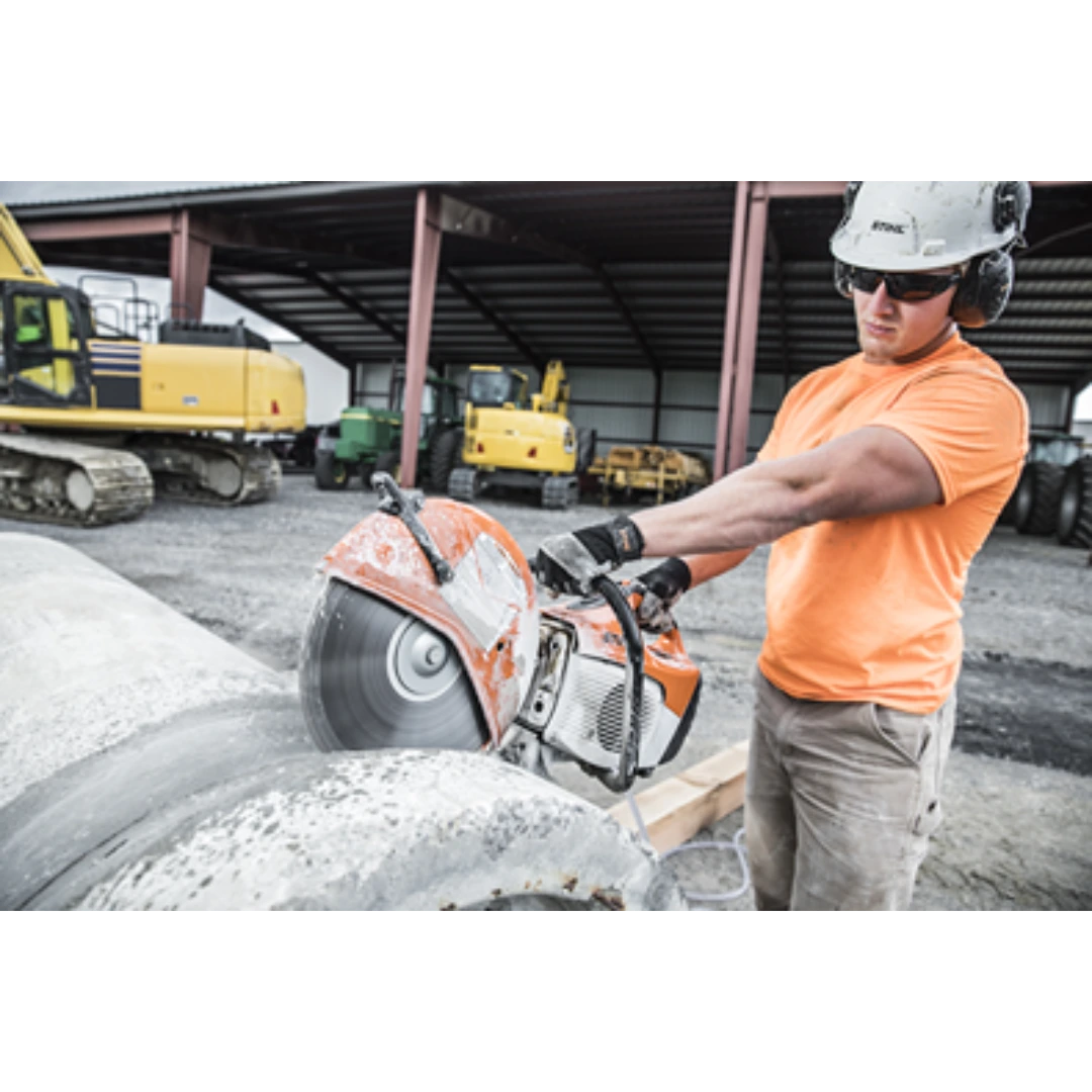 Worker in safety gear operating an orange and white power cutter cutting concrete pipe for home improvement tasks