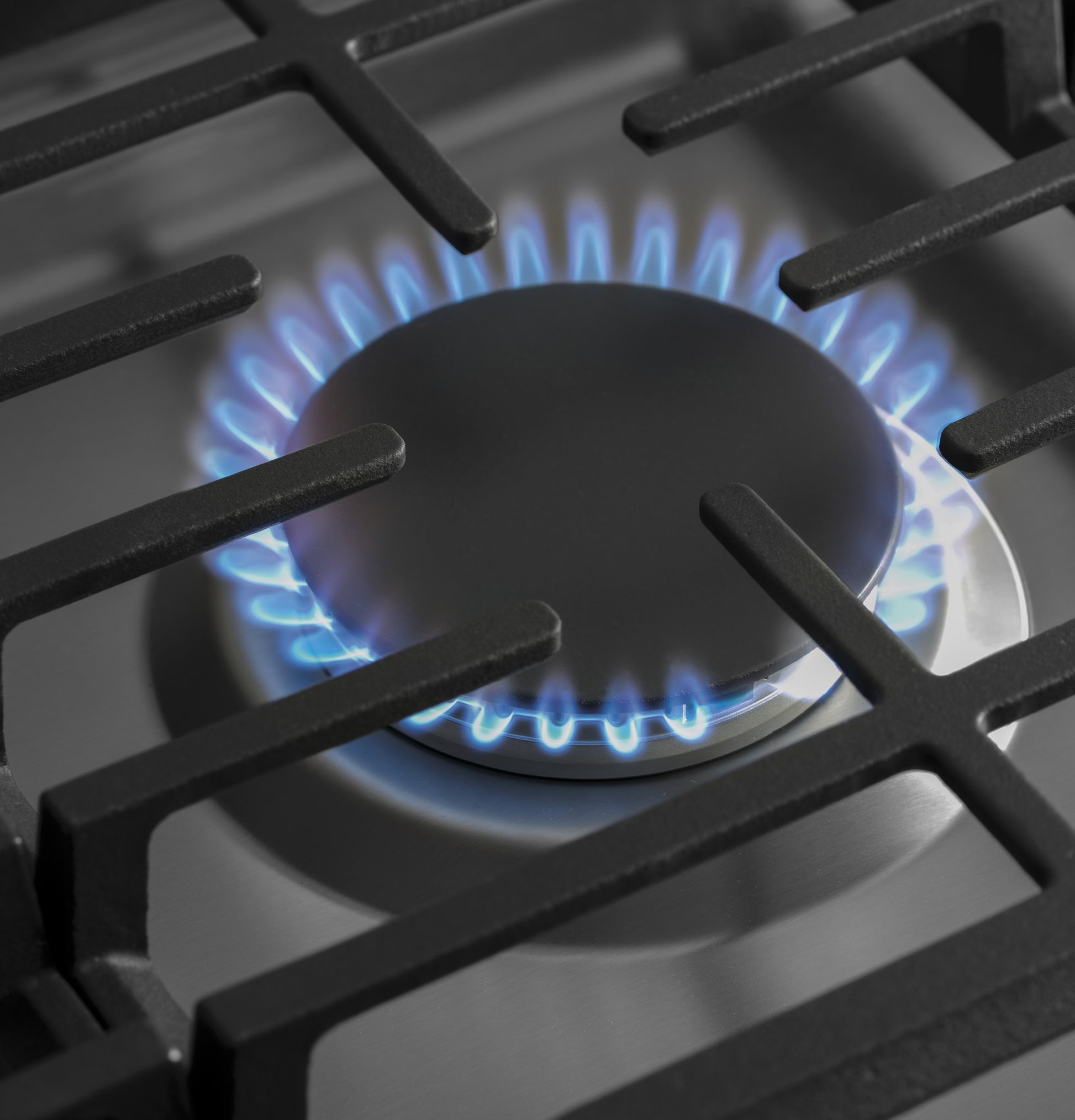 Close-up of blue flame burner on stainless steel gas cooktop in kitchen appliances and cooktops collection