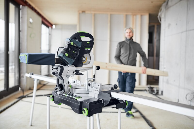Green and black sliding miter saw with dust bag setup, used in interior construction for precise wood cutting tasks