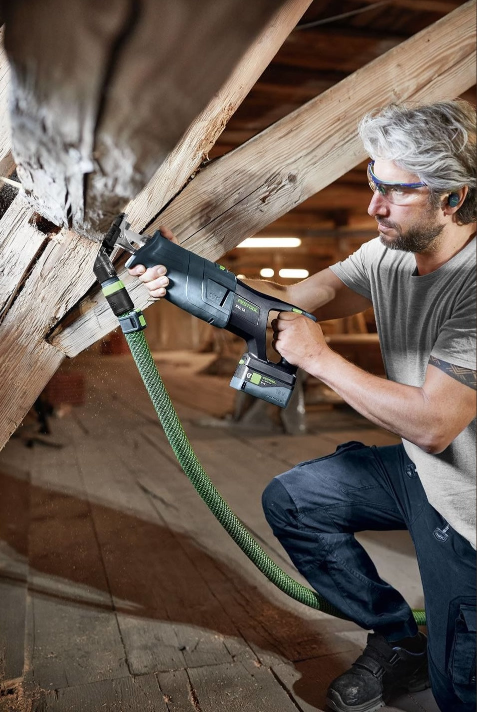 Person wearing safety glasses using a cordless sabre saw to cut a wooden beam in a home improvement setting