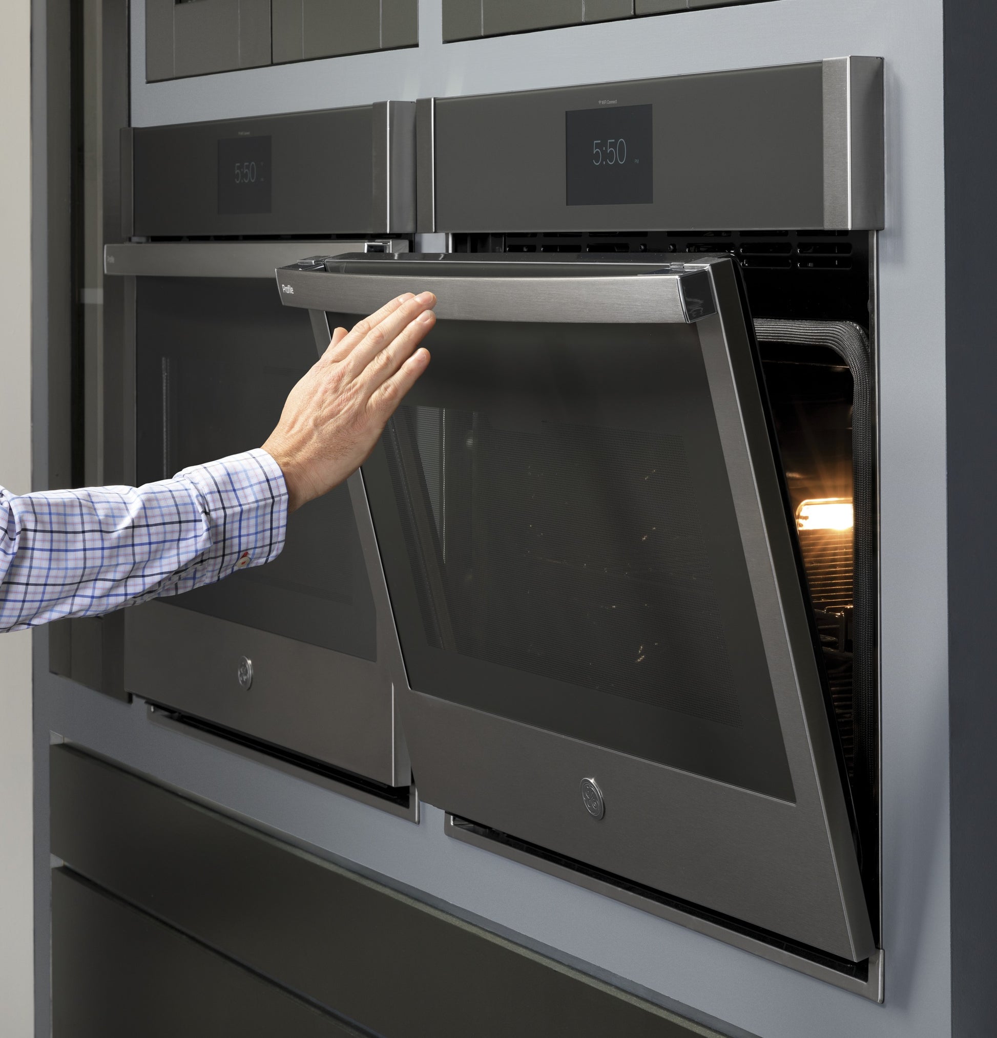 Person opening stainless steel convection double wall oven door in modern kitchen appliance setting