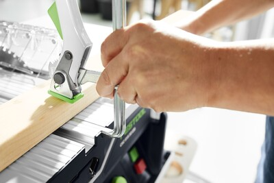 Hands securing a wood piece with a clamp on a Festool cordless table saw in a bright workshop setting