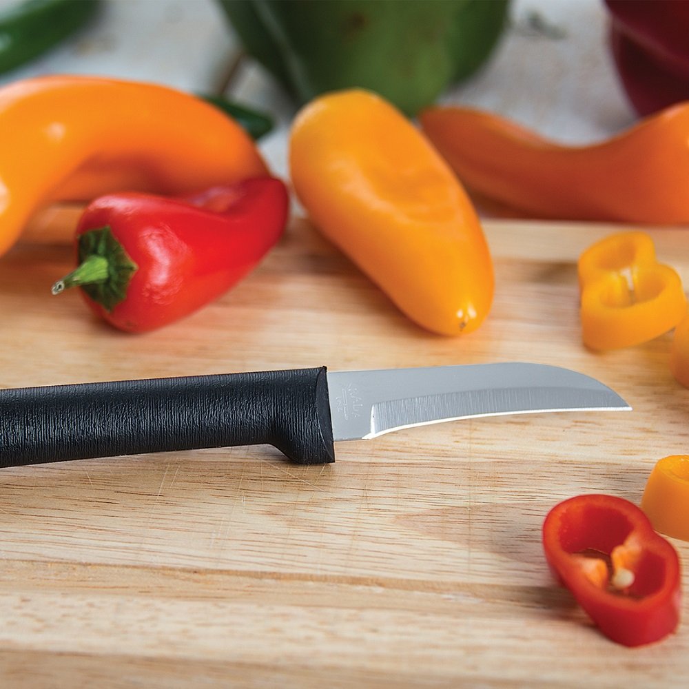 Small paring knife with curved blade and black handle on wooden board with sliced red and yellow peppers in kitchen utensils collection