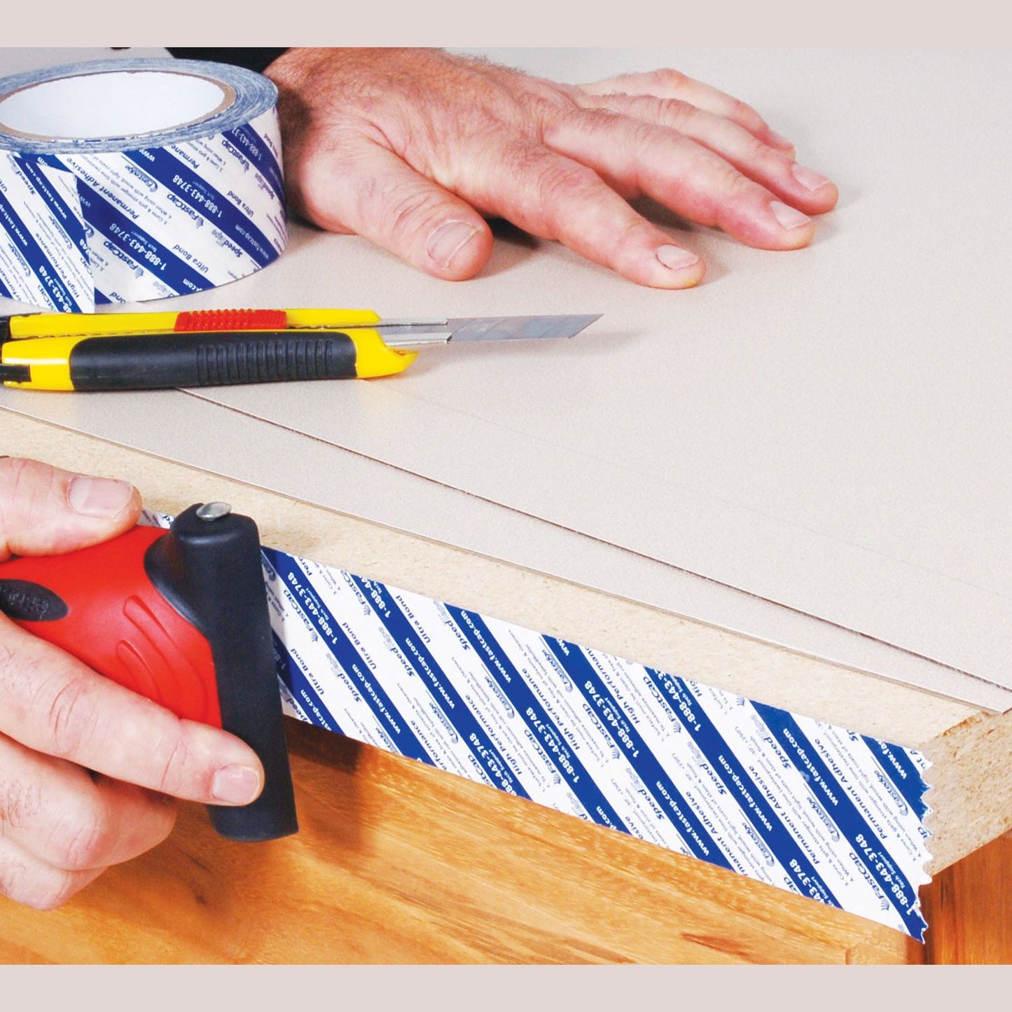 Applying blue and white branded adhesive tape to edge of wood panel using black roller tool for woodworking tasks