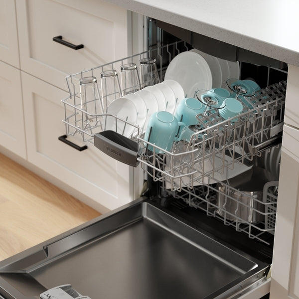 Open white dishwasher with upper rack loaded with clean glasses, plates, and teal mugs in kitchen setting