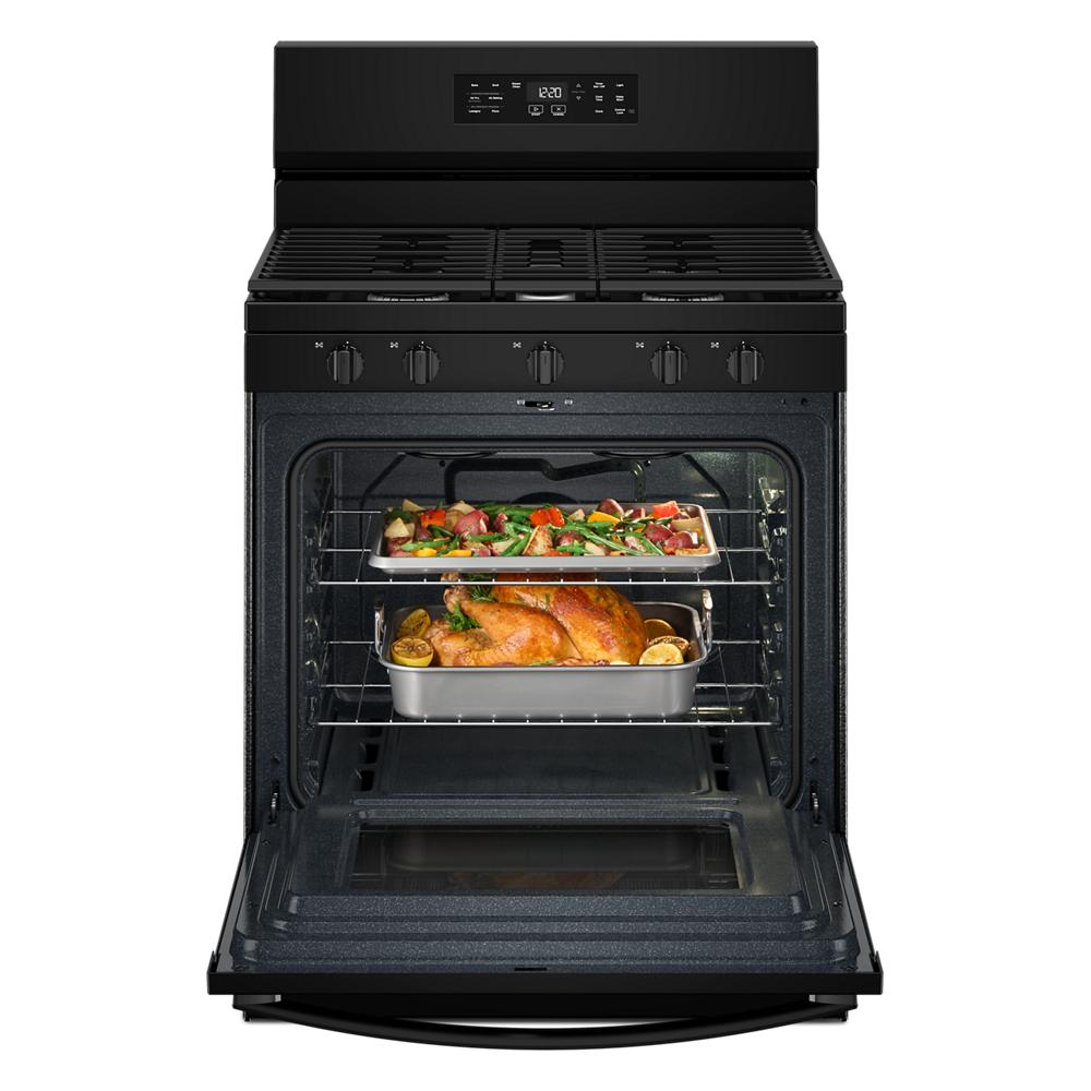 Open black gas range oven with cooked chicken and roasted vegetables inside, featuring control knobs and digital display panel