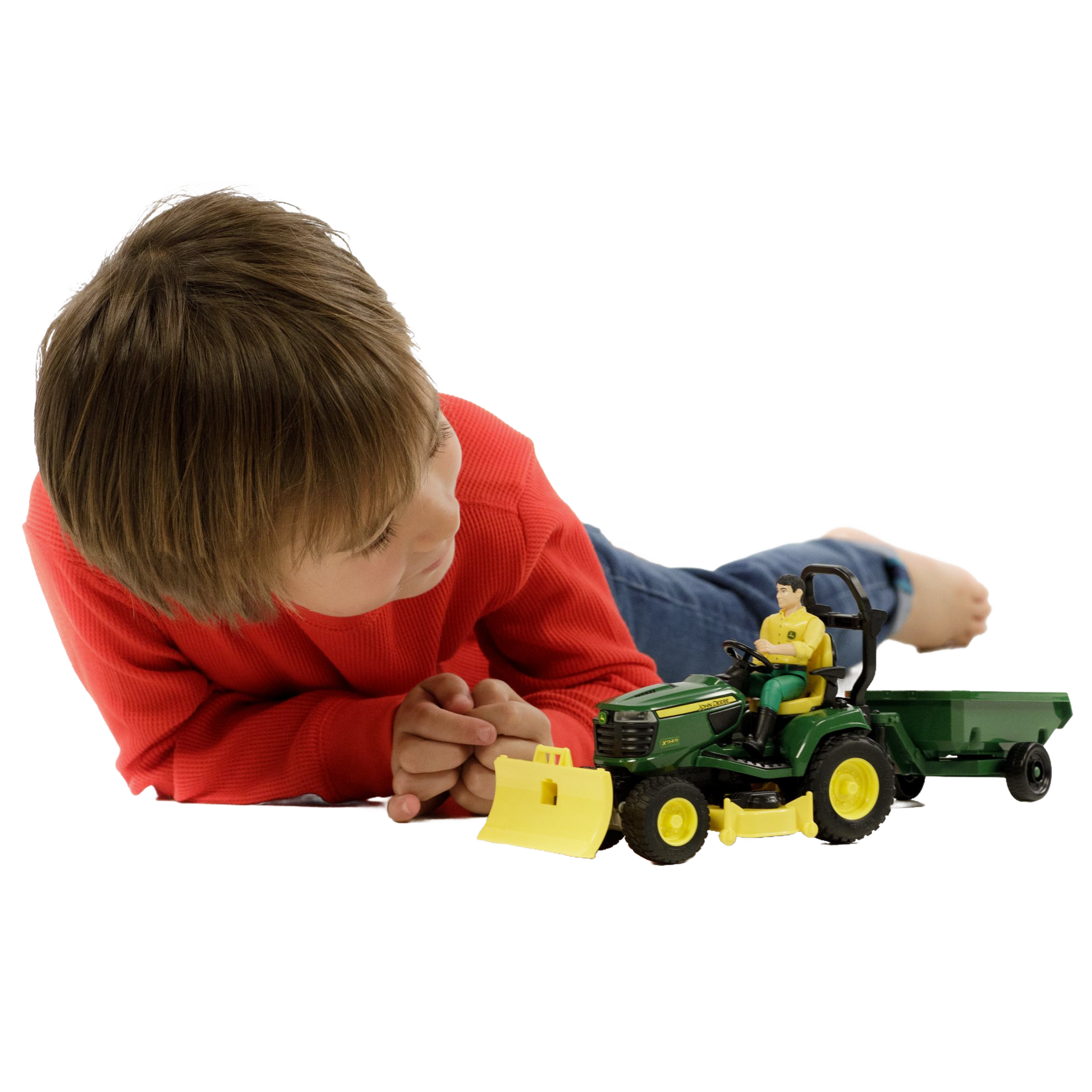 Child wearing red sweater lying down and playing with green and yellow toy tractor and attached trailer with figure