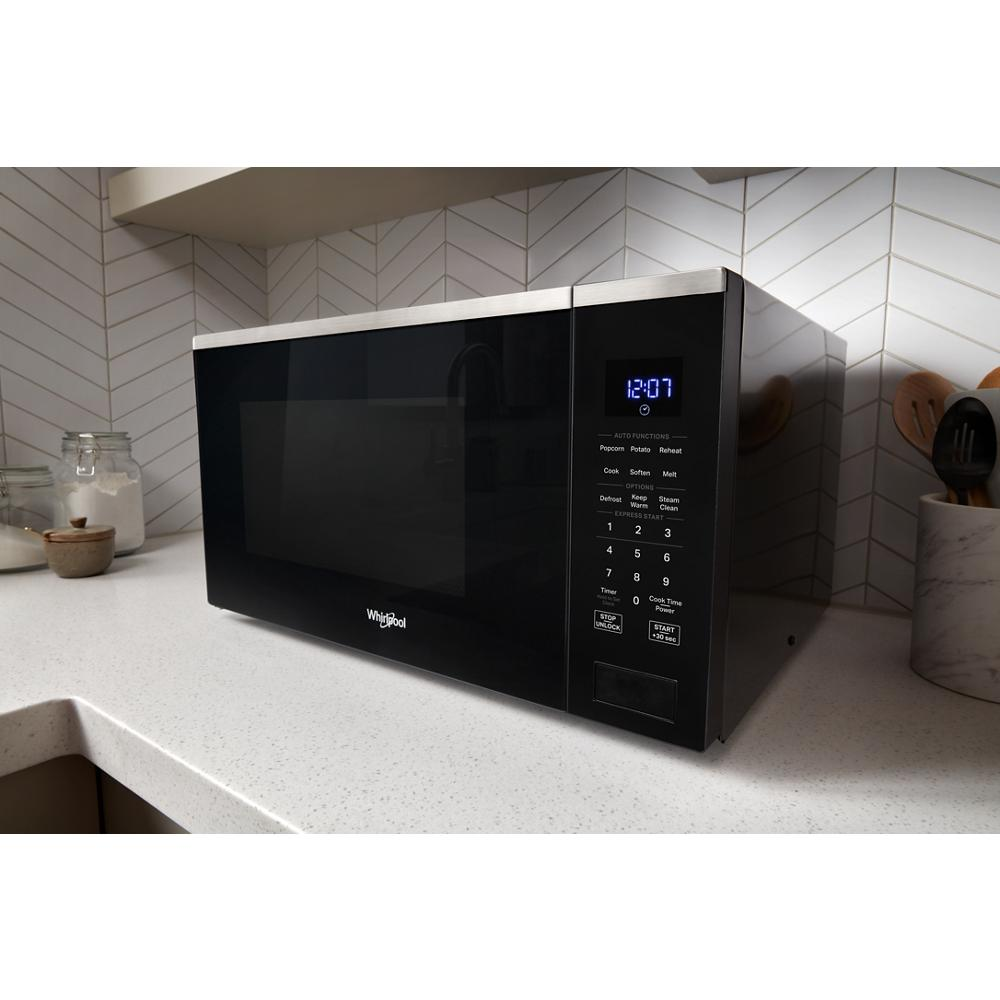 Black sensor microwave with digital display and control panel on white kitchen countertop in modern kitchen setting