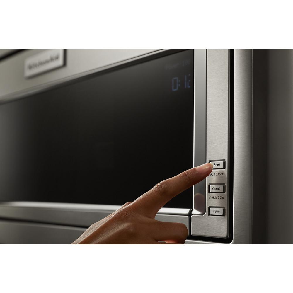Finger pressing start button on stainless steel built-in microwave control panel in modern kitchen appliances collection